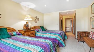 Un dormitorio con dos camas, una mesita de noche, una lámpara y un banco de madera.