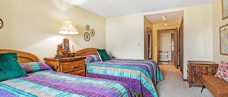 A bedroom with two beds, a nightstand, a lamp, and a wooden bench.