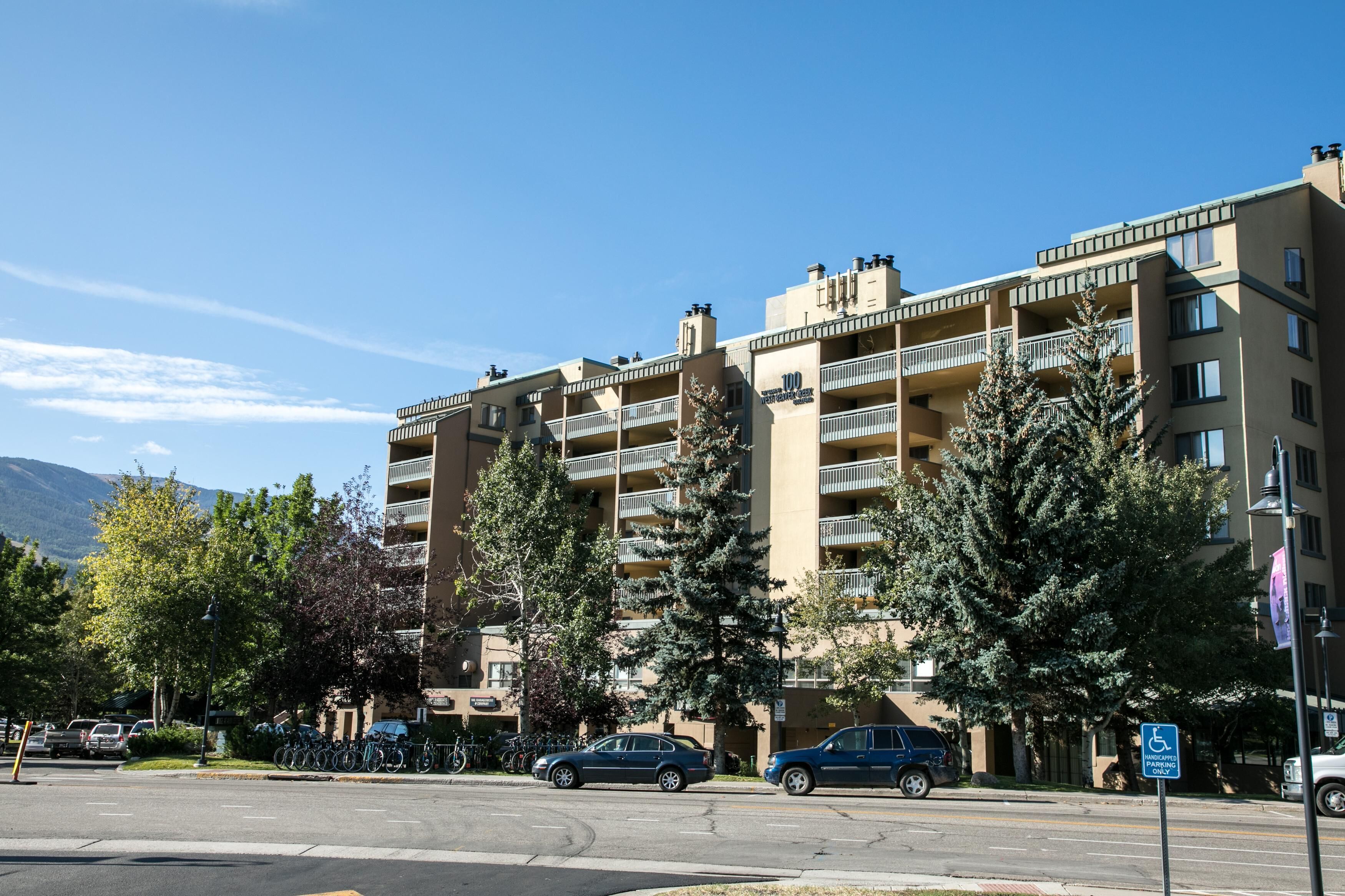 Un edificio de varios pisos con balcones, un estacionamiento y un cielo despejado.