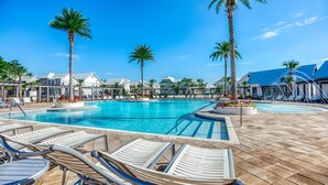 Ein Poolbereich mit Liegestühlen, Palmen und Gebäuden im Stil eines Resorts.