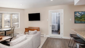 A living room with a sofa, a dining table, and a TV mounted on the wall. - Westwind 203 1BD Platinum Condo in Lionshead Village With A/C (Vail)