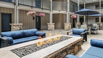 Un espace de détente extérieur à plusieurs niveaux, agrémenté de piliers en pierre, de sièges bleus et d’un foyer central.