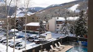 Uma área de piscina com espreguiçadeiras, uma banheira de hidromassagem e vista para montanhas cobertas de neve.