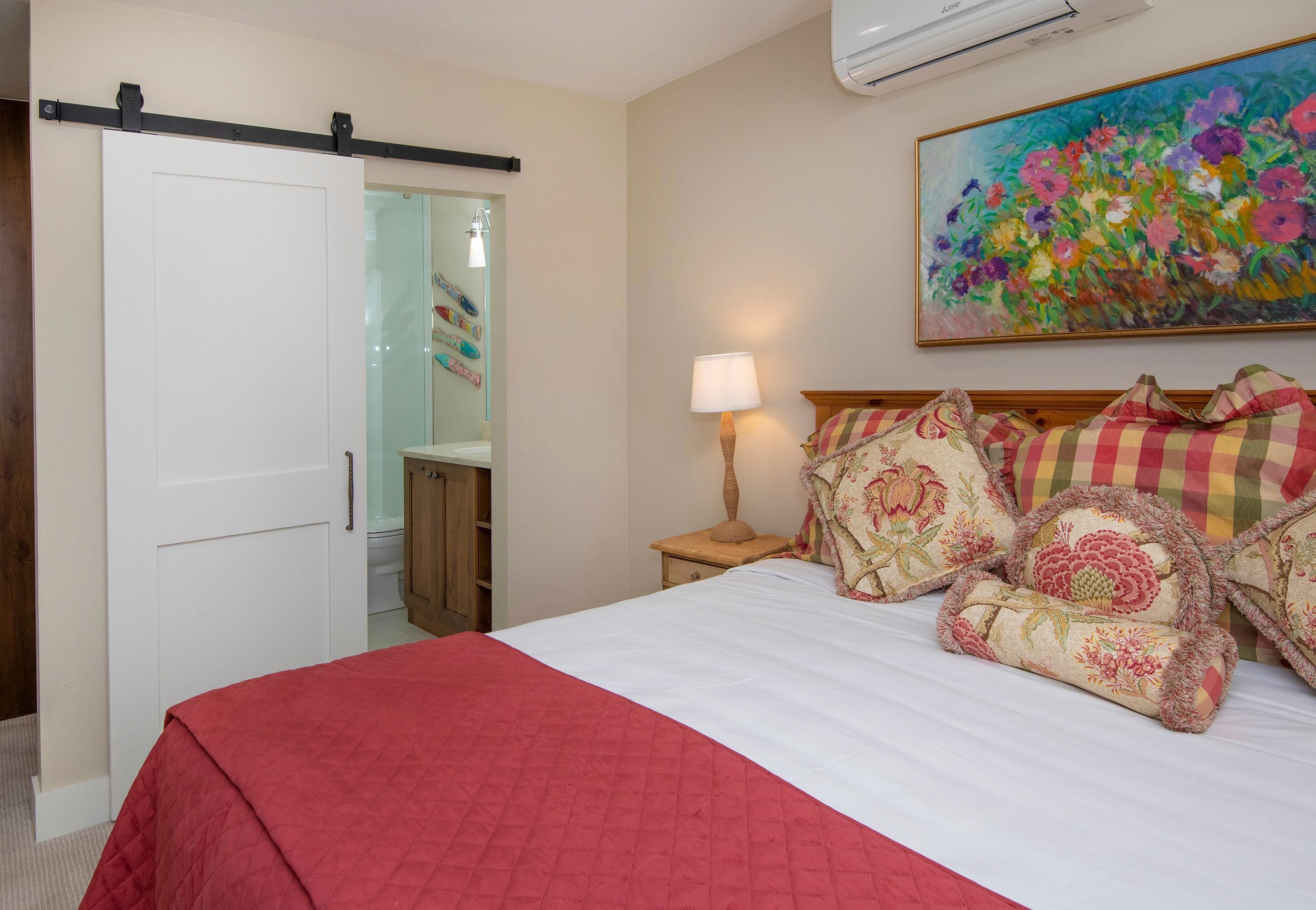 A bedroom with a bed, a nightstand, a lamp, a painting, and a sliding door.