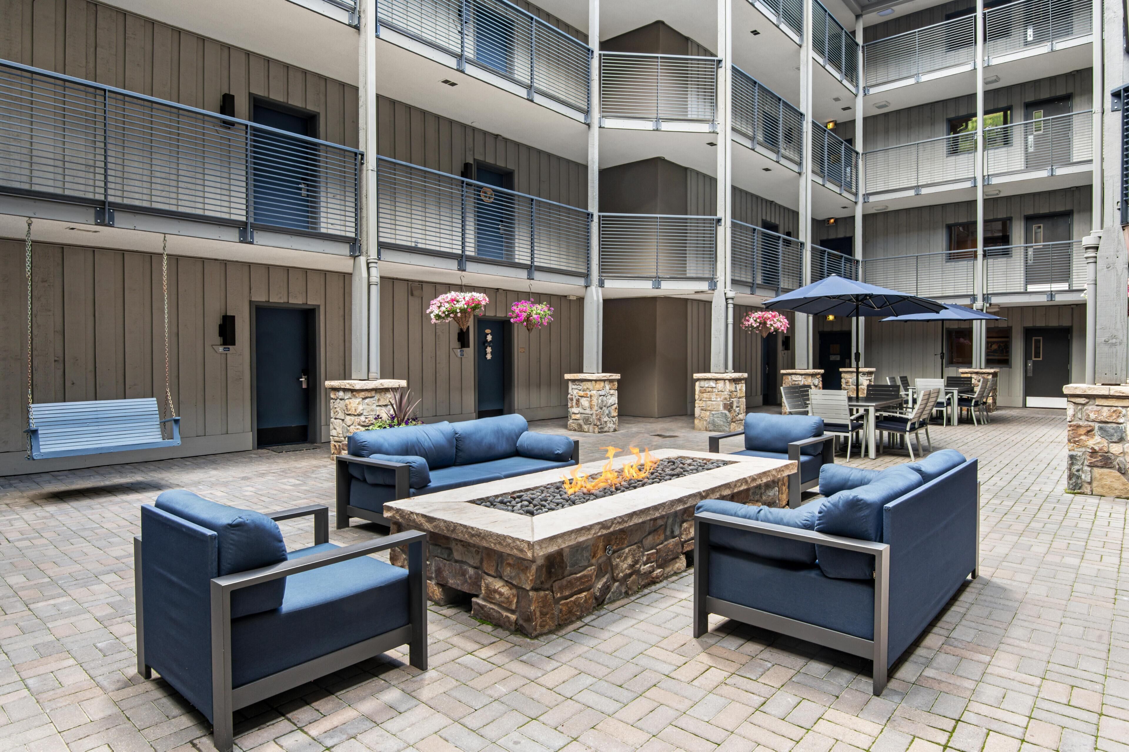 A multi-level outdoor patio with stone flooring, blue seating, a fire pit, and a dining area with umbrellas.
