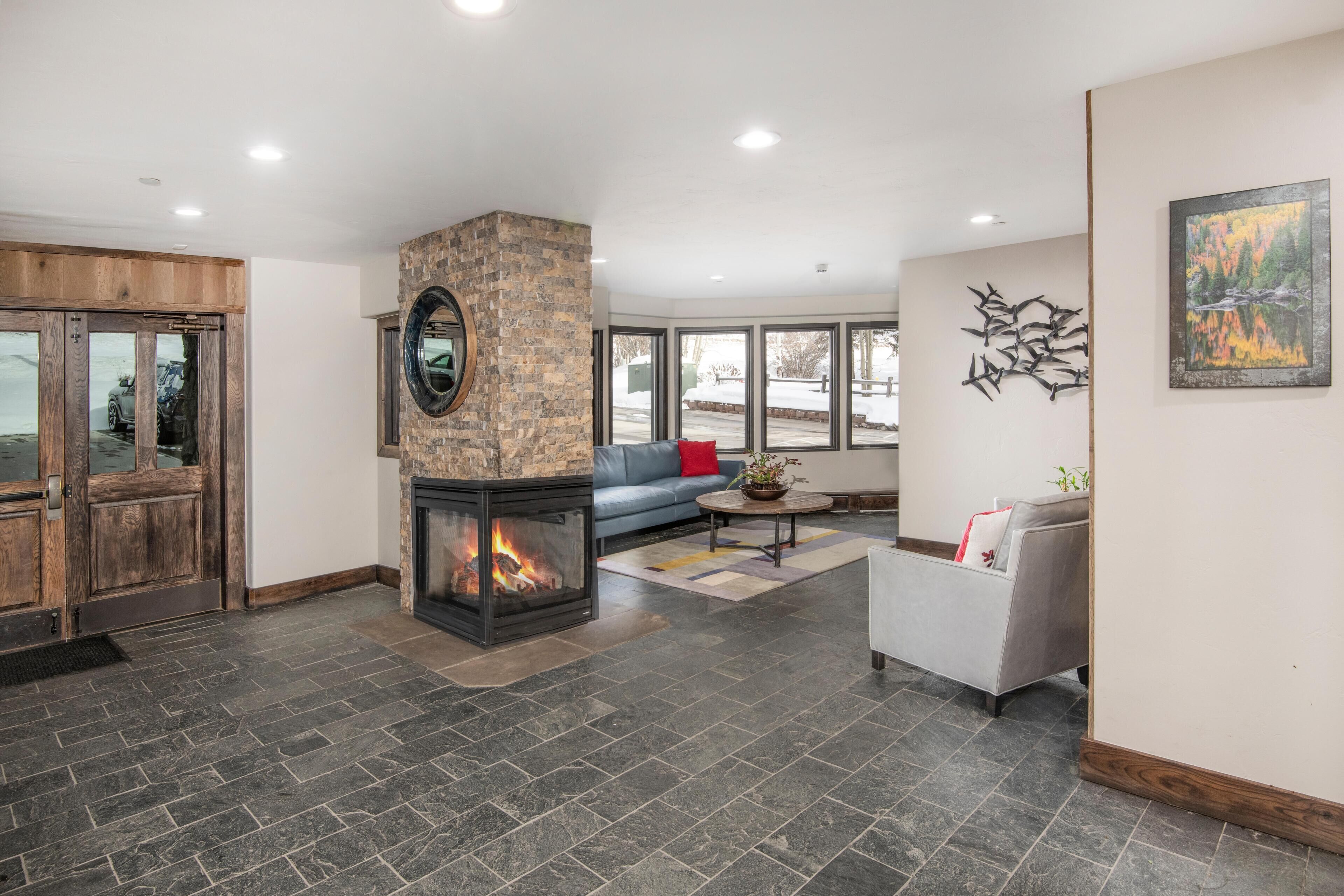 A modern living room with a stone fireplace, a blue sofa, a gray armchair, and a large window.