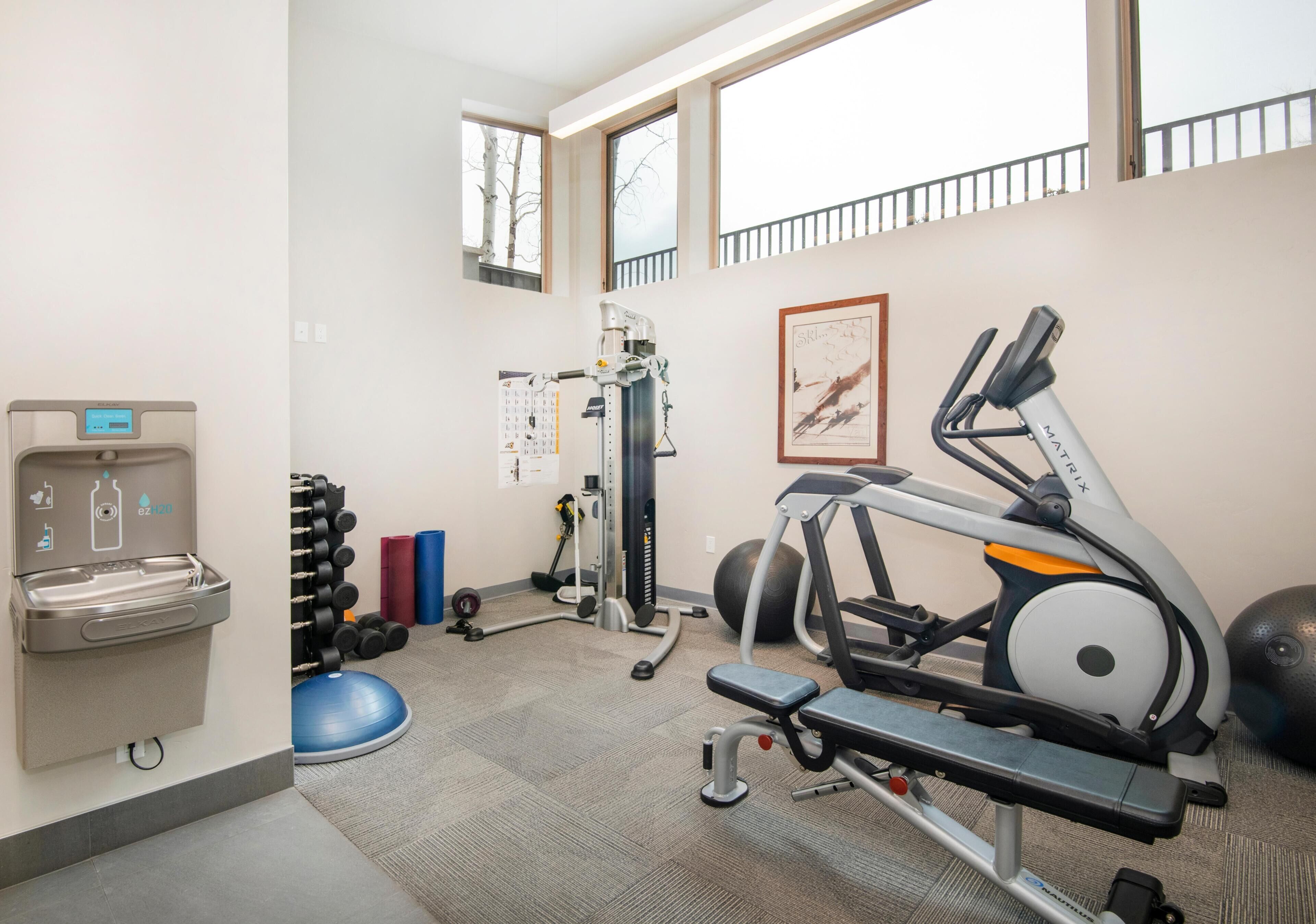Ein Fitnessraum mit Trainingsgeräten, einem Wasserspender und einem Kalender an der Wand.