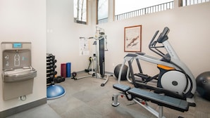 Uma academia com equipamentos de exercício, um bebedouro e um calendário na parede.