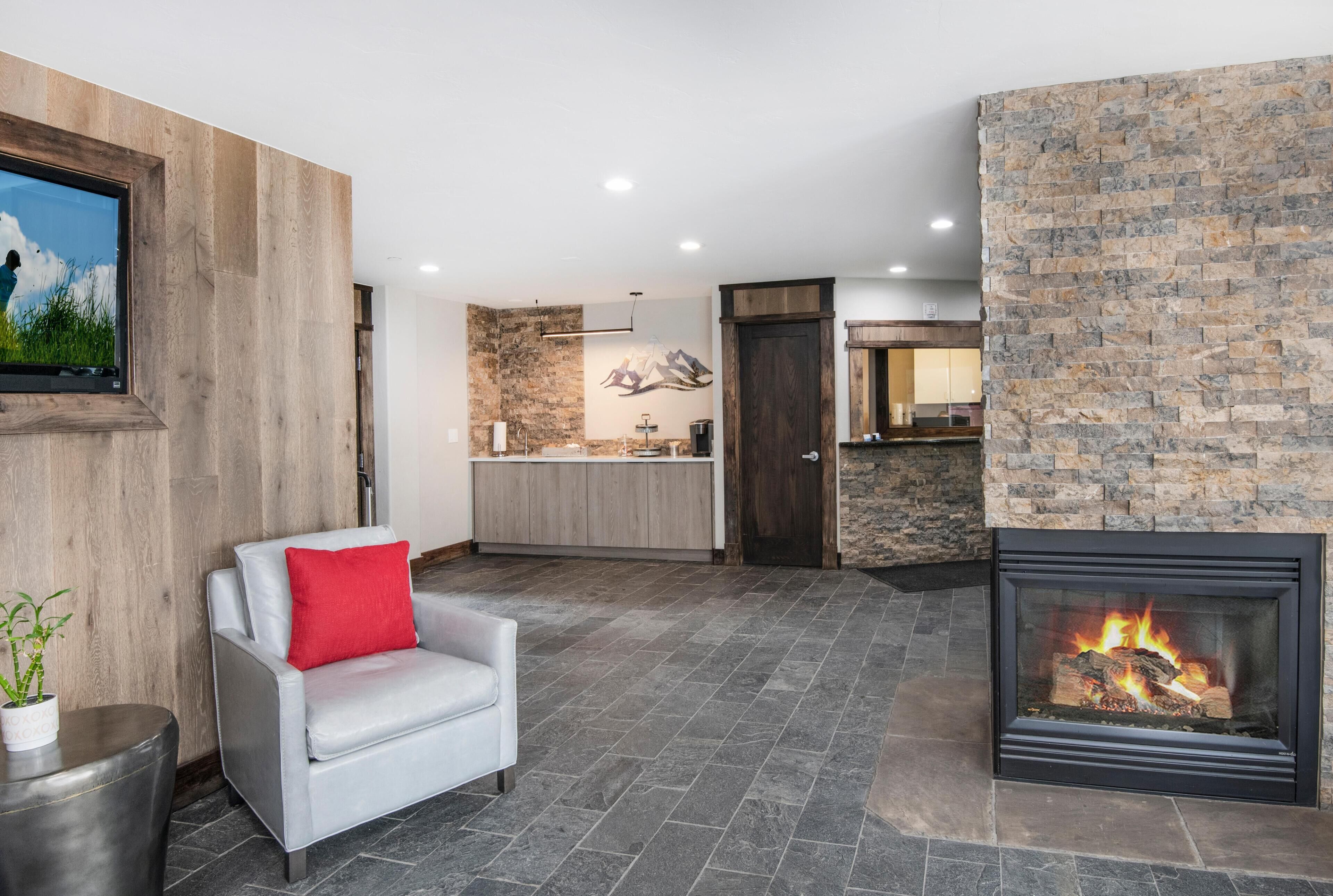 A modern living room with a fireplace, a stone wall, and a kitchen area in the background.