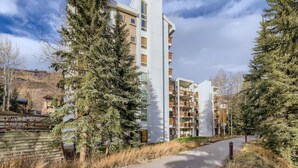 A modern multi-story residential building with balconies, surrounded by evergreen trees and a clear sky. - Treetops 5C, 3BD Ski-in Ski-out Condo (Vail)