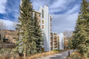 Ein modernes, mehrstöckiges Wohngebäude mit Balkonen, umgeben von immergrünen Bäumen und blauem Himmel.