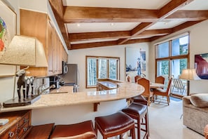 A kitchen with wooden beams, a large window, and a bar area with stools. - Treetops 5C, 3BD Ski-in Ski-out Condo (Vail)