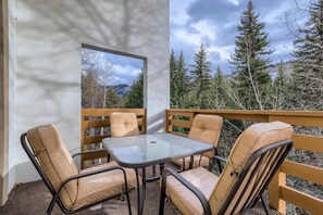 Ein Balkon mit einem Glastisch und vier gepolsterten Stühlen, mit Blick auf eine bewaldete Landschaft und Berge im Hintergrund.
