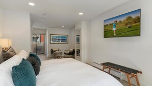 Ein Schlafzimmer mit einem großen Bett, einer Bank, einem Fernseher und einer Tür, die auf einen Balkon führt.