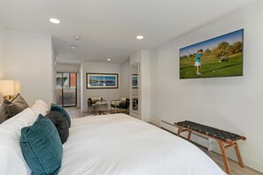 Ein Schlafzimmer mit einem großen Bett, einer Bank, einem Fernseher und einer Tür, die auf einen Balkon führt.