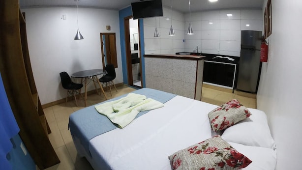 Una habitación con cama, escritorio, silla, kitchenette y televisión.