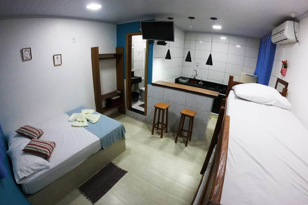 A compact room with a bed, a small kitchenette, a TV, and a bathroom.