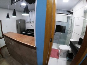 Una cocina con encimera, refrigerador y estufa. Hay un baño con inodoro, lavabo y ducha.