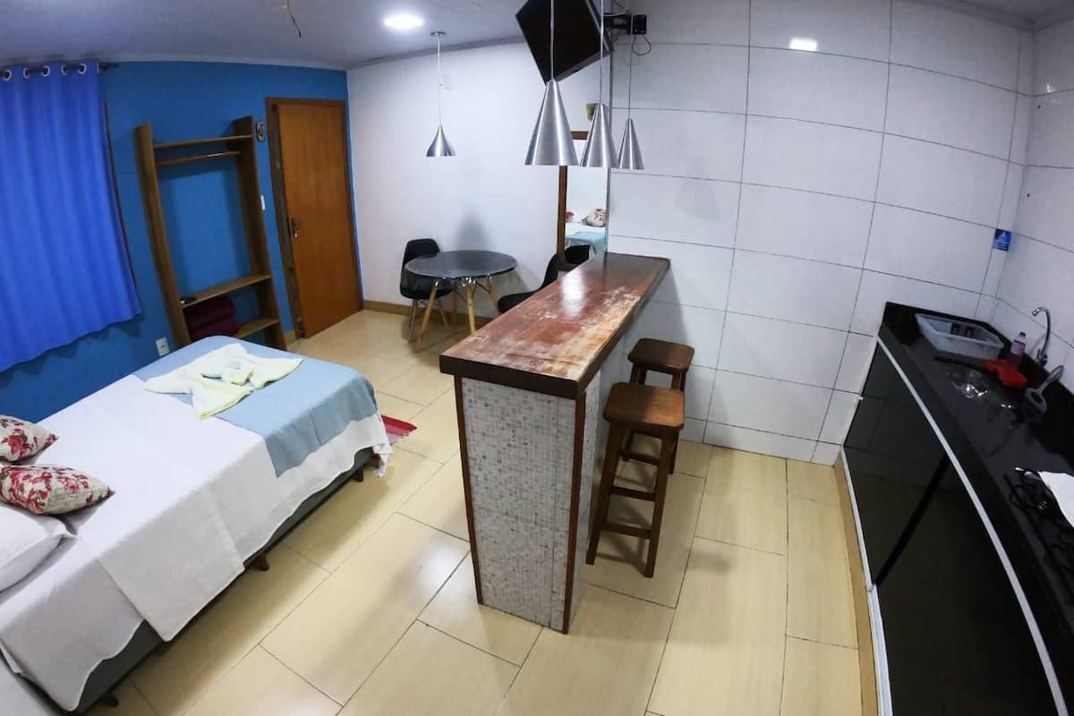 A compact room with a bed, a small kitchenette, a dining table, and a bar area.