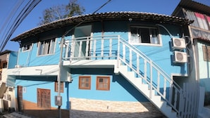Un edificio de dos pisos con fachada azul, una escalera blanca y un pequeño porche.