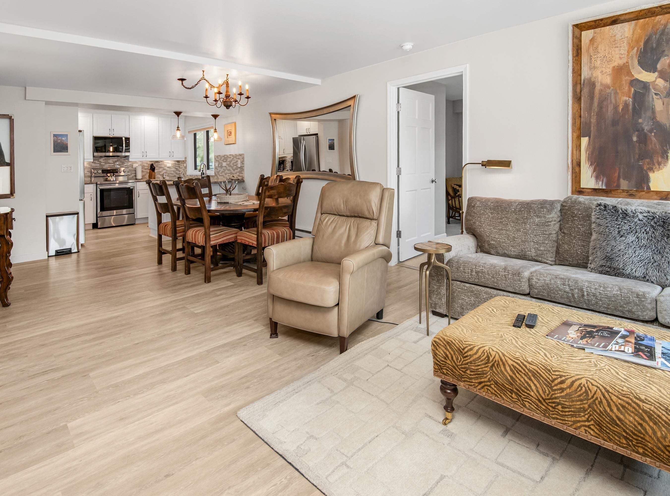 Una sala moderna con sofá, sillón, mesa de comedor y cocina al fondo.