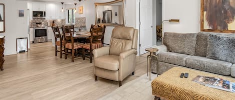 Una sala moderna con sofá, sillón, mesa de comedor y cocina al fondo.
