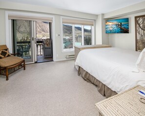 Ein Schlafzimmer mit einem großen Bett, einem Sessel, Blick durch die Tür und einem Bild an der Wand.