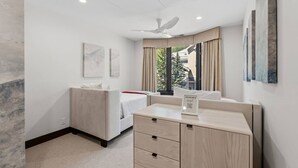 Habitación de hotel con cama, escritorio, silla, ventilador de techo y obras de arte en las paredes.