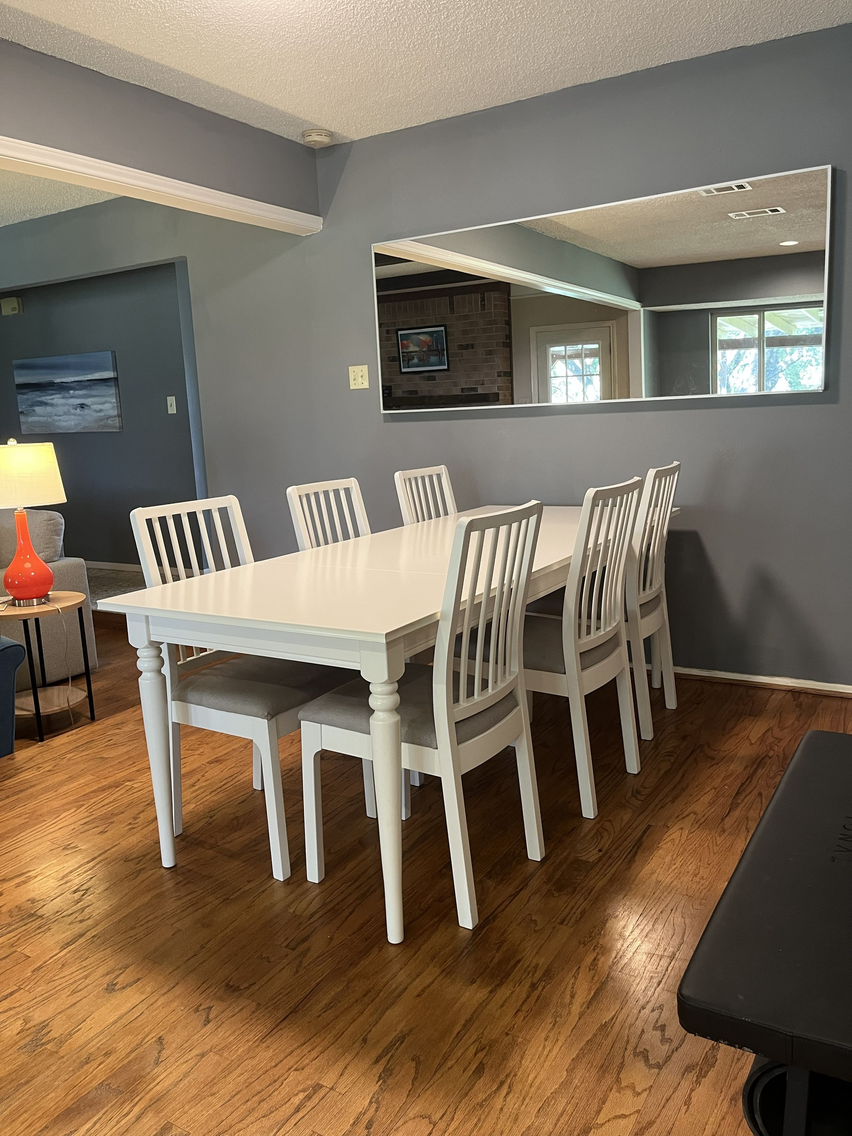 A dining area with a white table and chairs, a red lamp, and a painting on the wall.