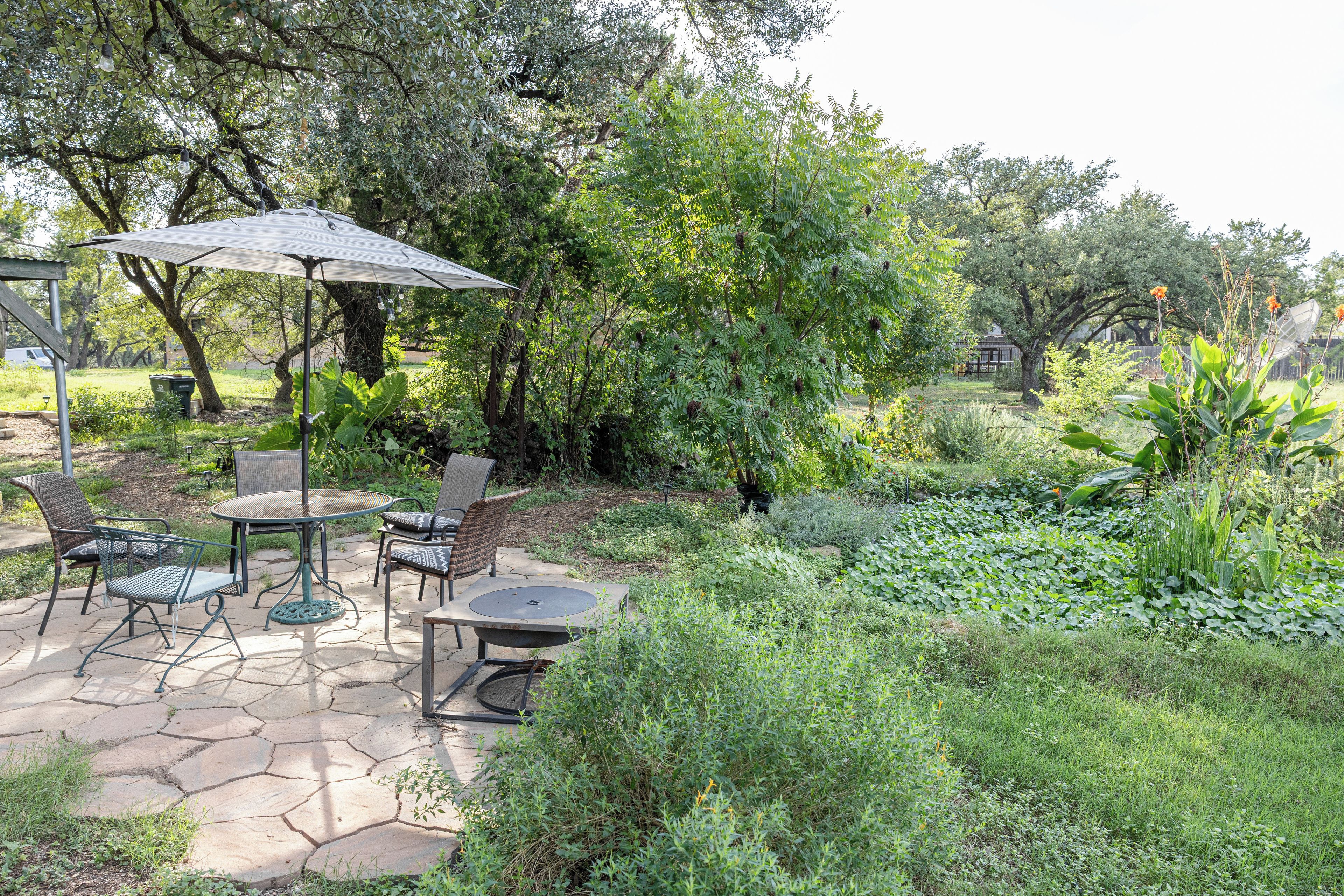 An outdoor patio with a table and chairs, surrounded by lush greenery and trees.