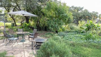 An outdoor patio with a table and chairs, surrounded by lush greenery and trees.