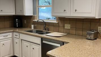 A kitchen with white cabinets, a Bosch dishwasher, a toaster, and a window with a view of trees.