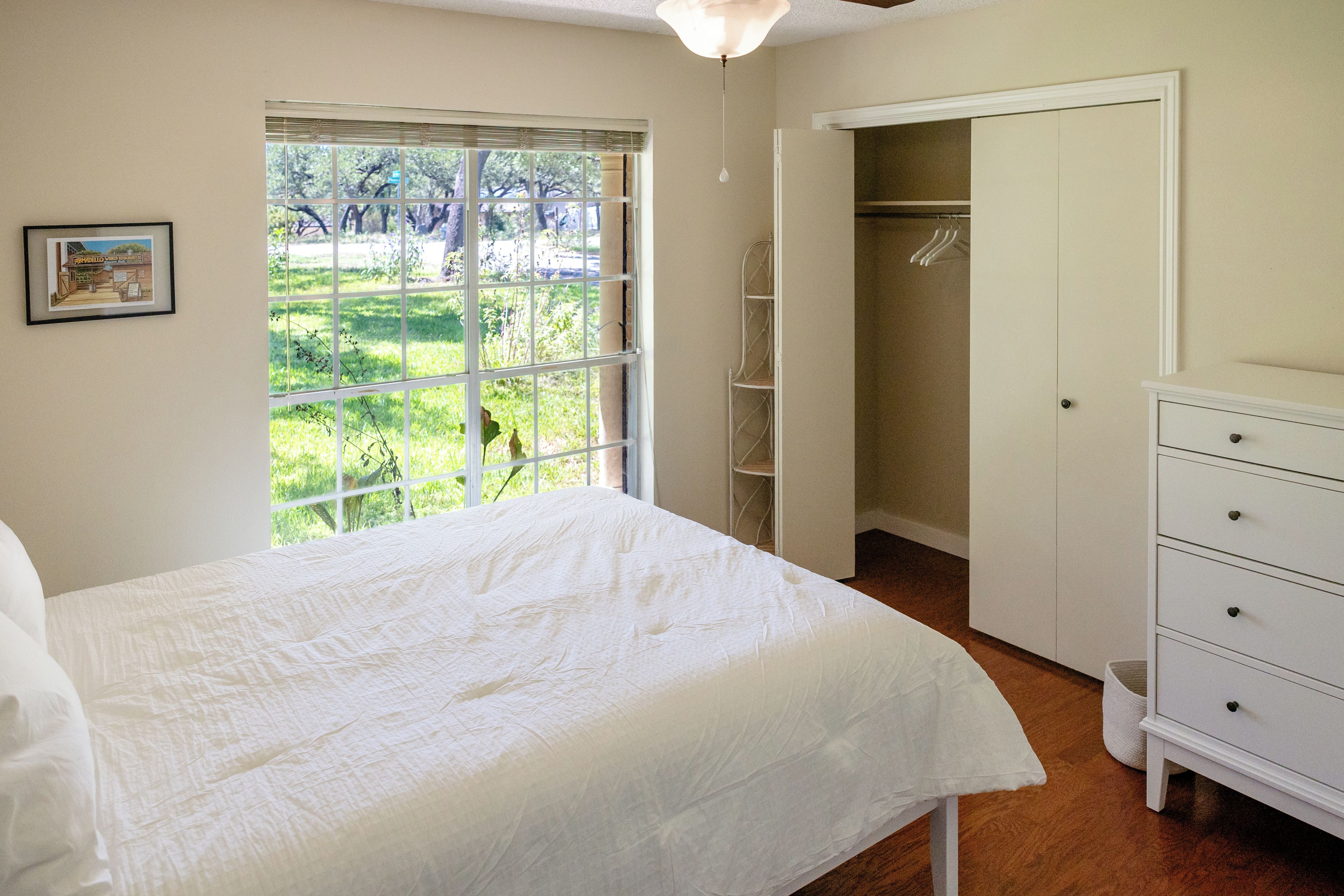 A bedroom with a bed, a wardrobe, and a window with a view of greenery.