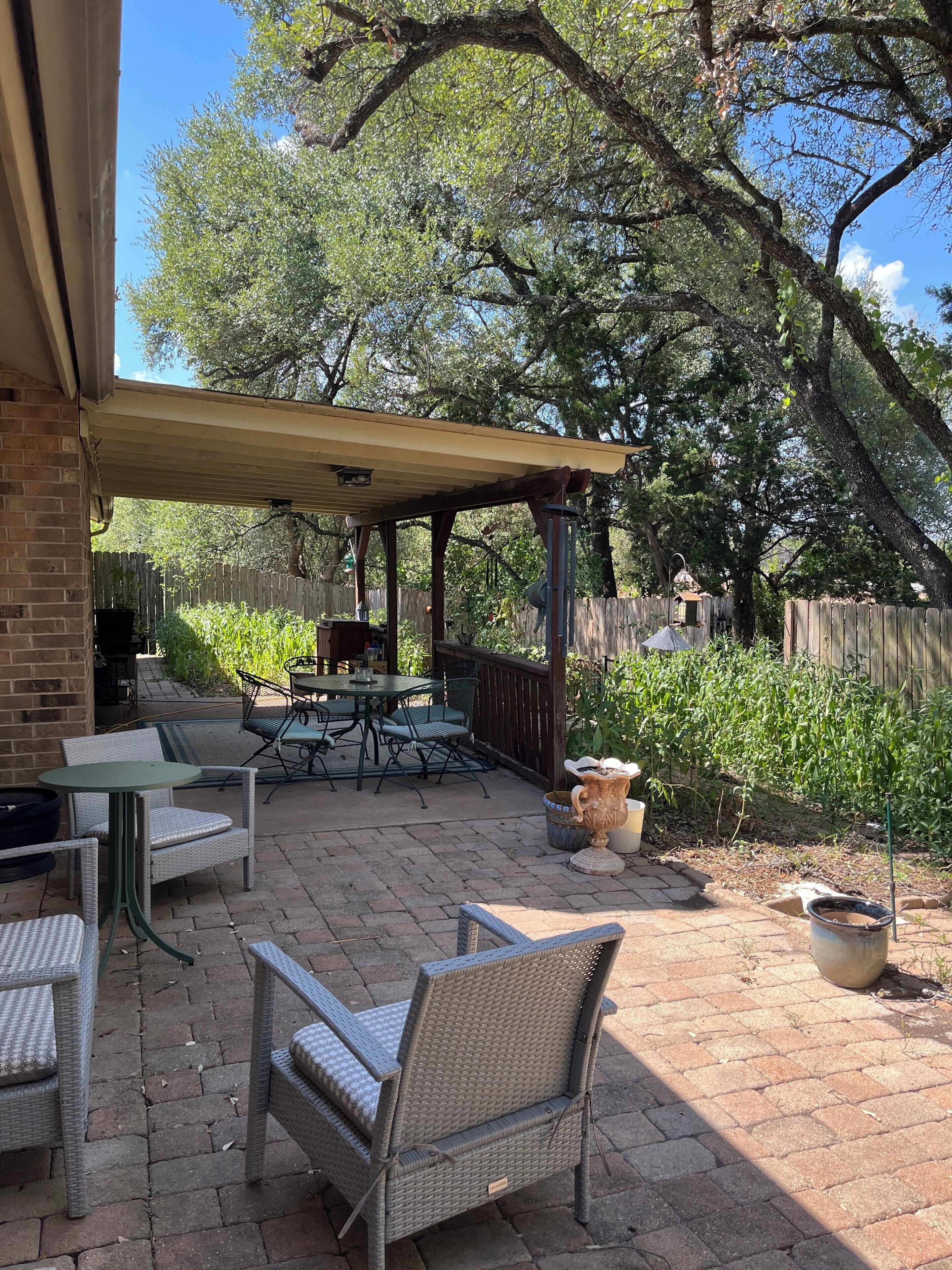 An outdoor patio with wicker furniture, a covered seating area, and a wooden fence.