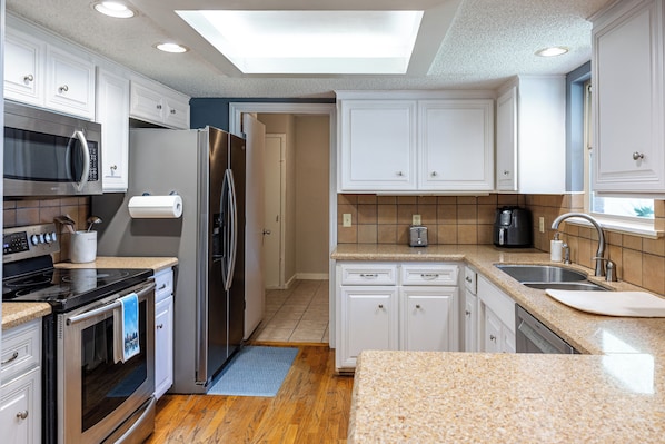 A modern kitchen with white cabinetry, stainless steel appliances, a built-in microwave, a refrigerator, a dishwasher, and a coffee maker.