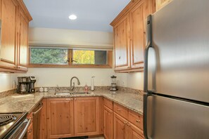 A kitchen with wooden cabinets, a stainless steel refrigerator, a window, and a granite countertop. - Snow Fox 201, 2BD Modern Vail Condo (Vail)
