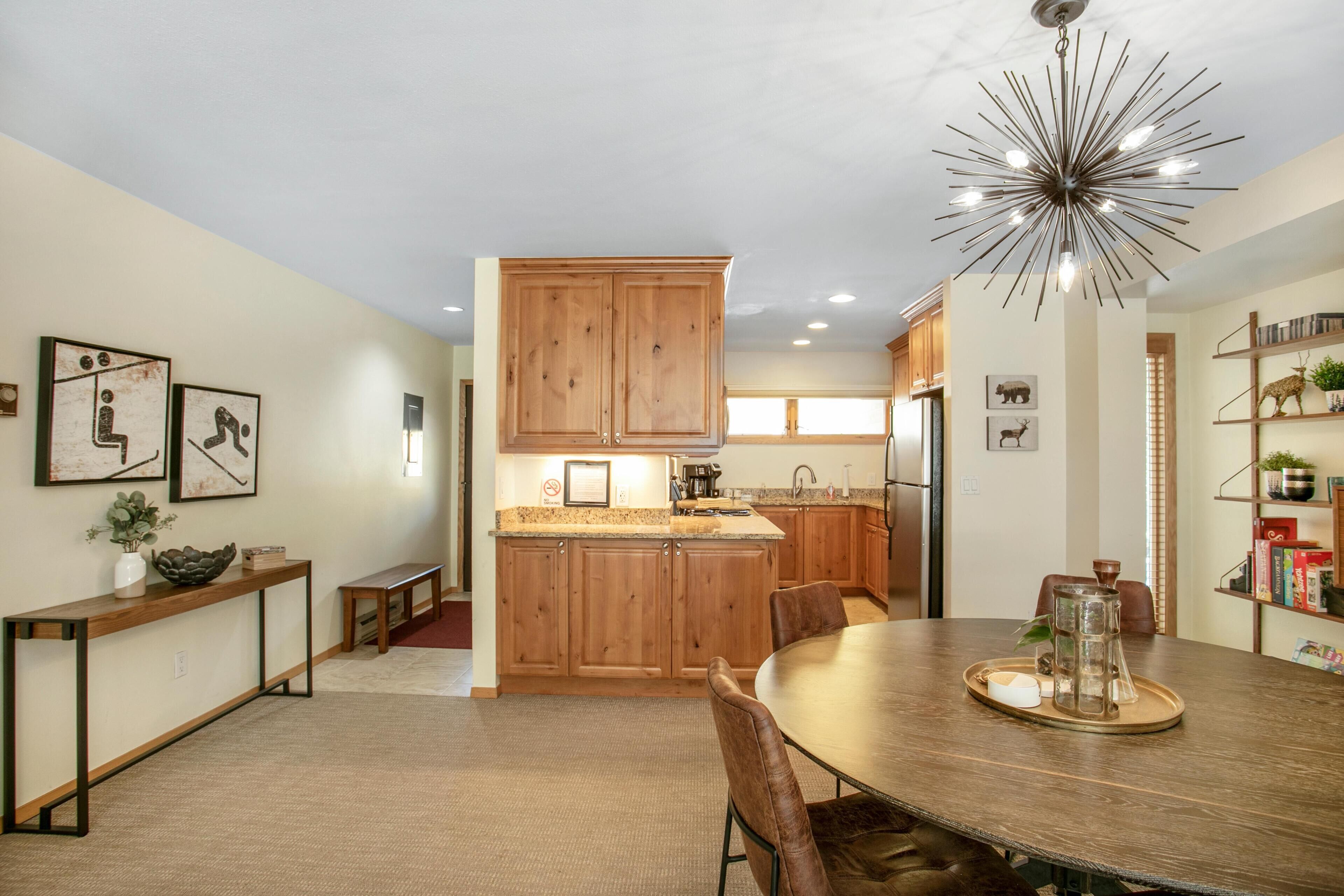A modern kitchen with wooden cabinets, a dining table, and a unique chandelier.