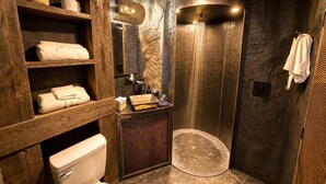 A bathroom with a stone wall, wooden shelves, a toilet, a sink, and a shower. - Cozy Cave - With a View (Lancaster)