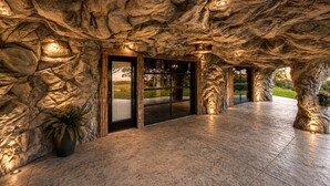 A stone facade with a door and windows, a potted plant, and a pathway leading to an outdoor area. - Cozy Cave - With a View (Lancaster)