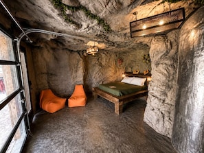 A room with a stone wall, a bed, orange chairs, and a window.