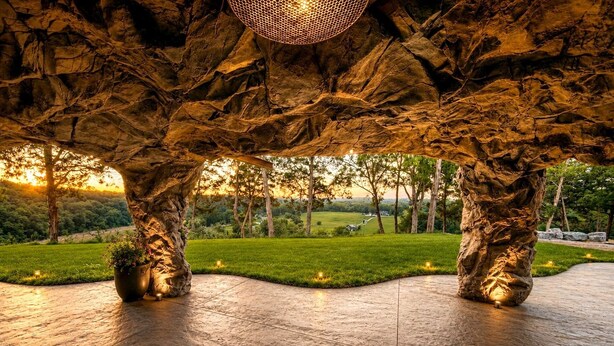 A stone-tiled floor with a unique rock-like structure overhead, a potted plant, and a view of a green landscape. - Cozy Cave - With a View (Lancaster)