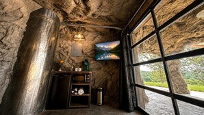 A room with a stone wall, a small kitchenette, a window with a mountain view, and a mounted painting. - Cozy Cave - With a View (Lancaster)