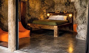 Une chambre à coucher au style rustique, avec un mur en pierre, un cadre de lit en bois et une couverture verte.