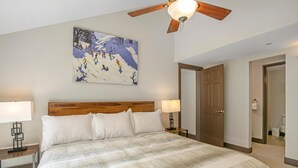 A hotel room with a large bed, wooden headboard, a ceiling fan, a painting on the wall, and a door leading to a bathroom. - Treetops Plaza One, 2BD Ski-in Ski-out Condo (Vail)