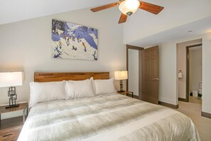 Ein Hotelzimmer mit einem großen Bett, einem Holzkopfende, einem Deckenventilator, einem Bild an der Wand und einer Tür zu einem Badezimmer.