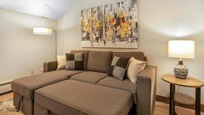 A modern bedroom with a large bed, a painting on the wall, and a small table with a lamp. - Treetops Plaza One, 2BD Ski-in Ski-out Condo (Vail)