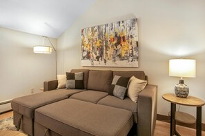 Ein modernes Schlafzimmer mit einem großen Bett, einem Gemälde an der Wand und einem kleinen Tisch mit einer Lampe.