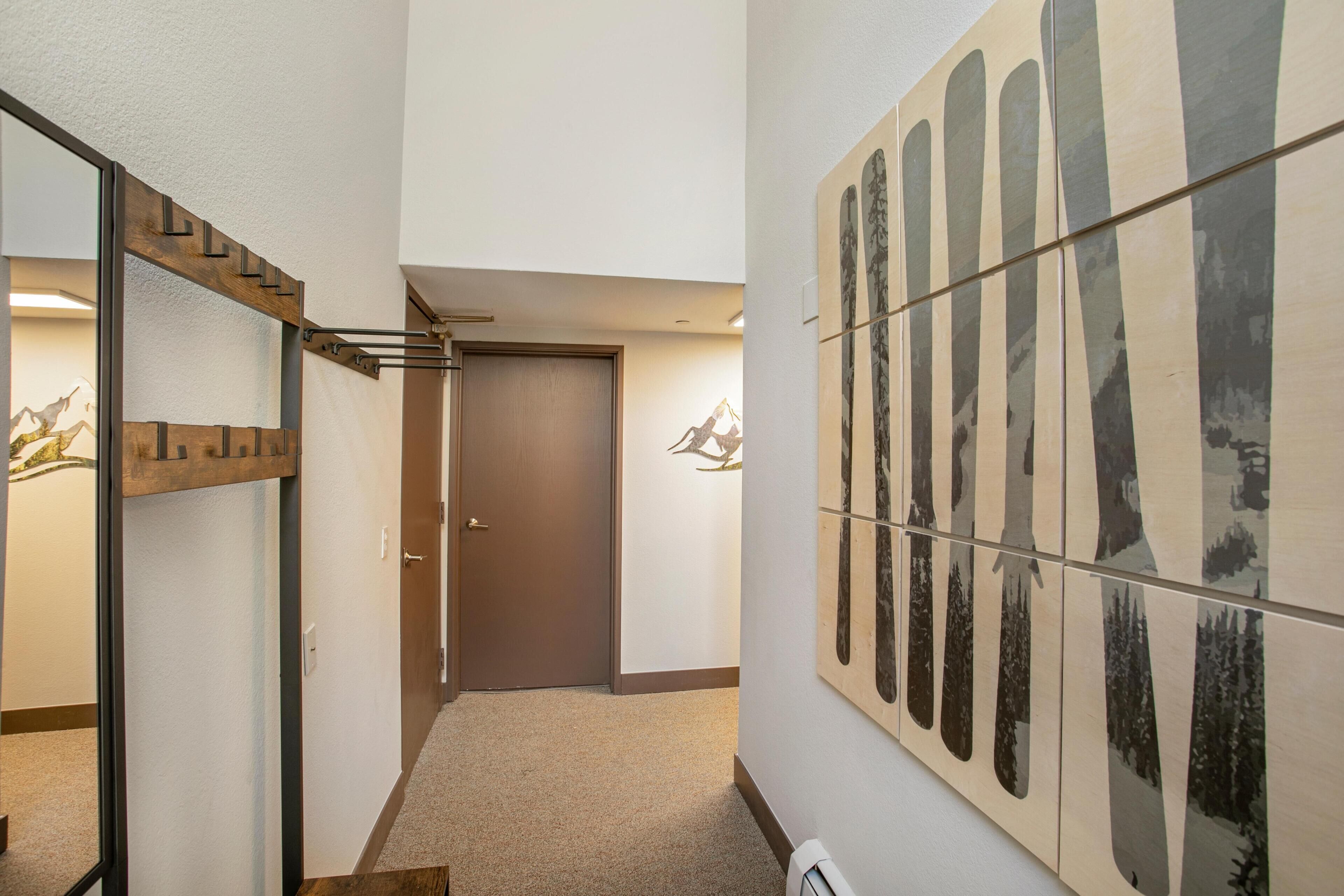 A hallway with a wooden staircase, a door, and a wall with vertical patterned artwork.
