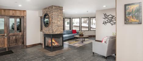 A modern living room with a stone fireplace, a blue sofa, a gray armchair, and a large window.