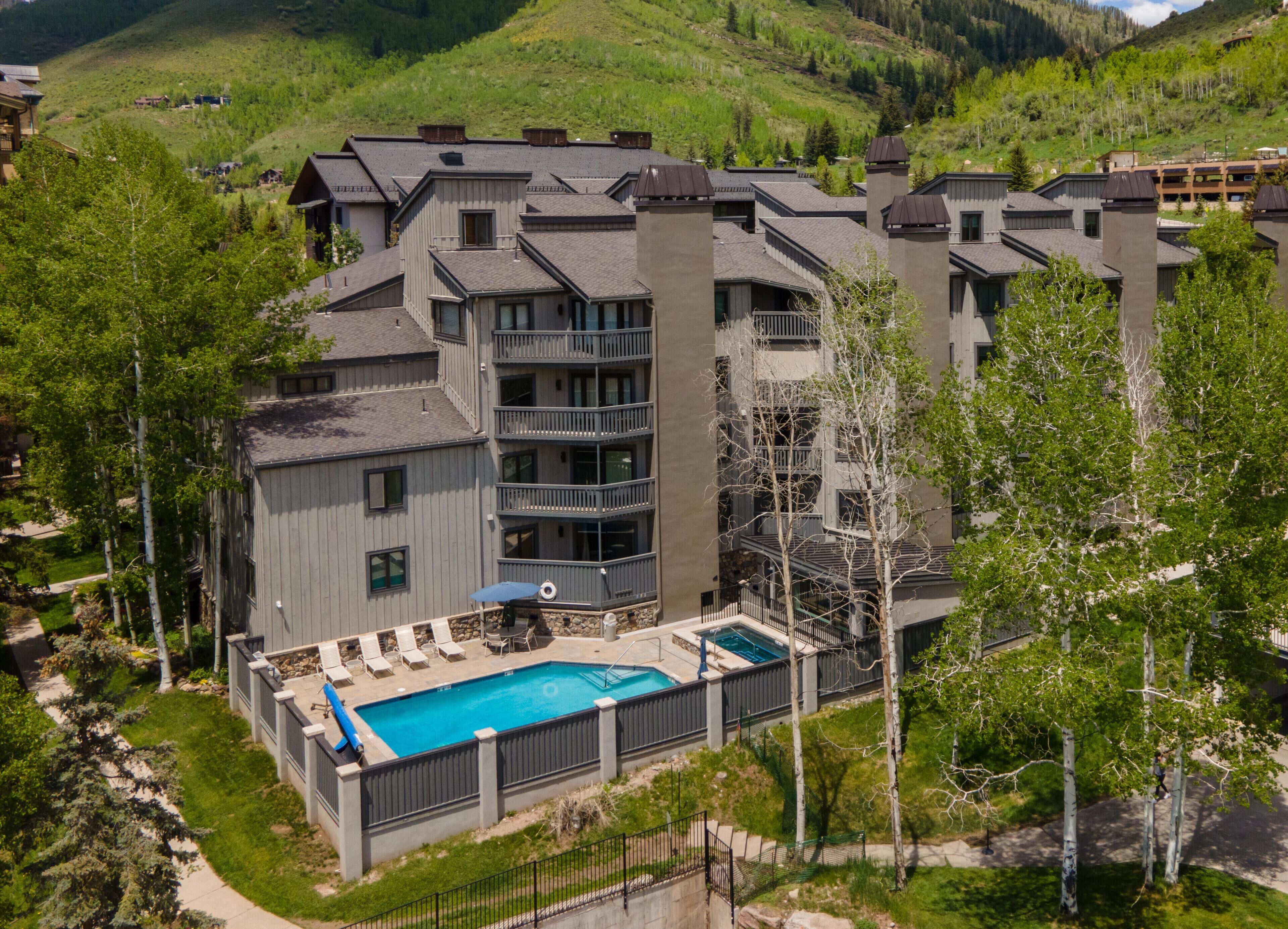 Un hotel de varios pisos con piscina, mobiliario exterior y vistas a las colinas circundantes.